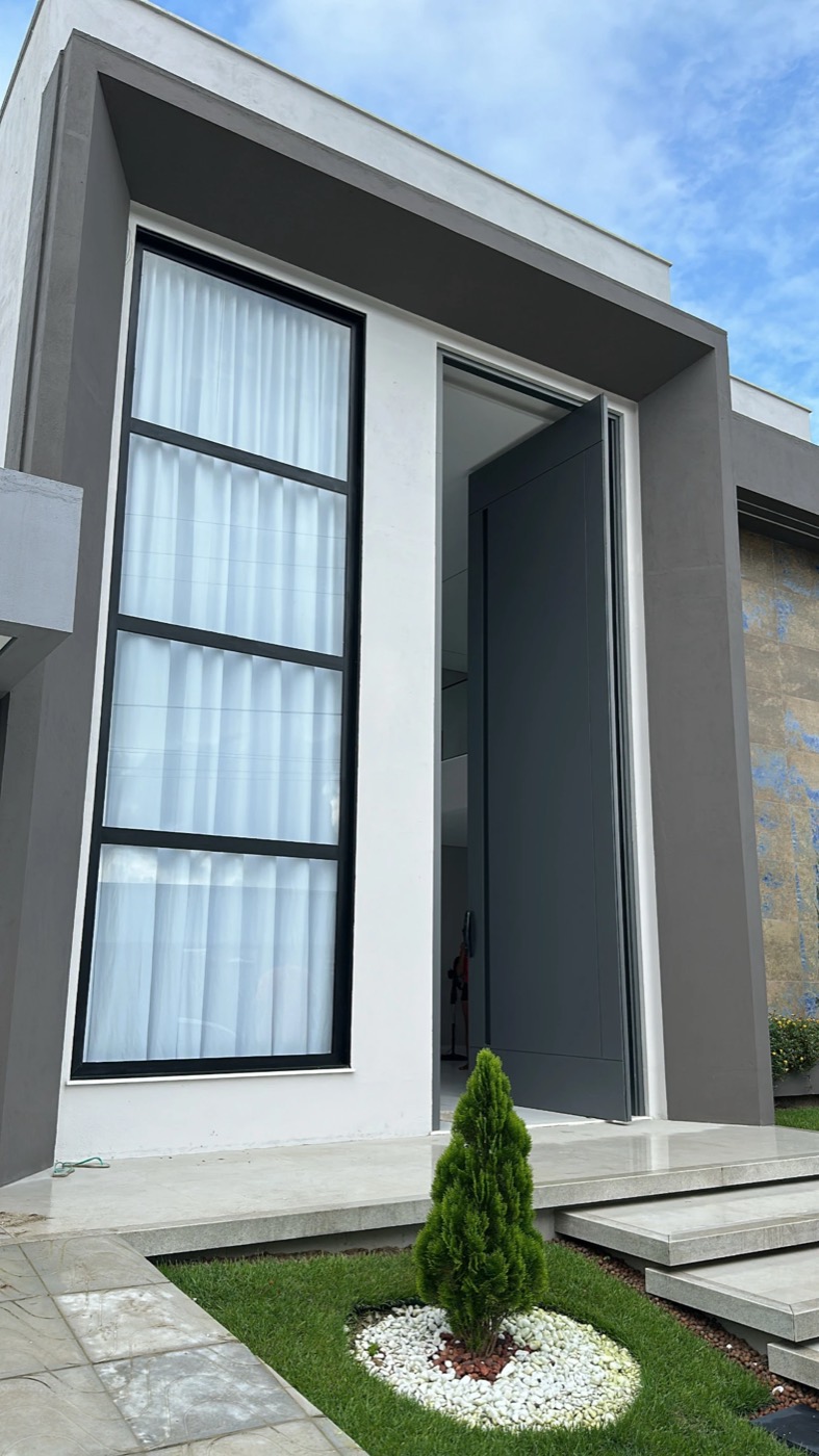 Fachada residencial com porta pivotante em alumínio e janela do piso ao teto